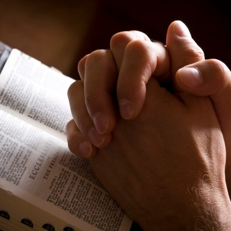Hands closed in prayer on an open bible